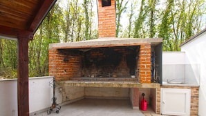 Un horno de ladrillo al aire libre con un lavabo y un mueble de almacenamiento, rodeado por una terraza de madera y un suelo de piedra.