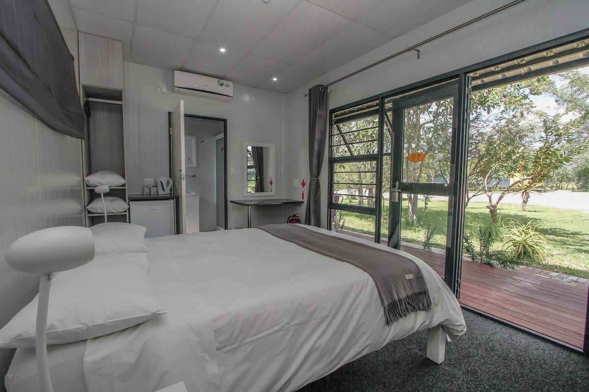 A modern bedroom with a large bed, a desk, and a window with a view of a garden.