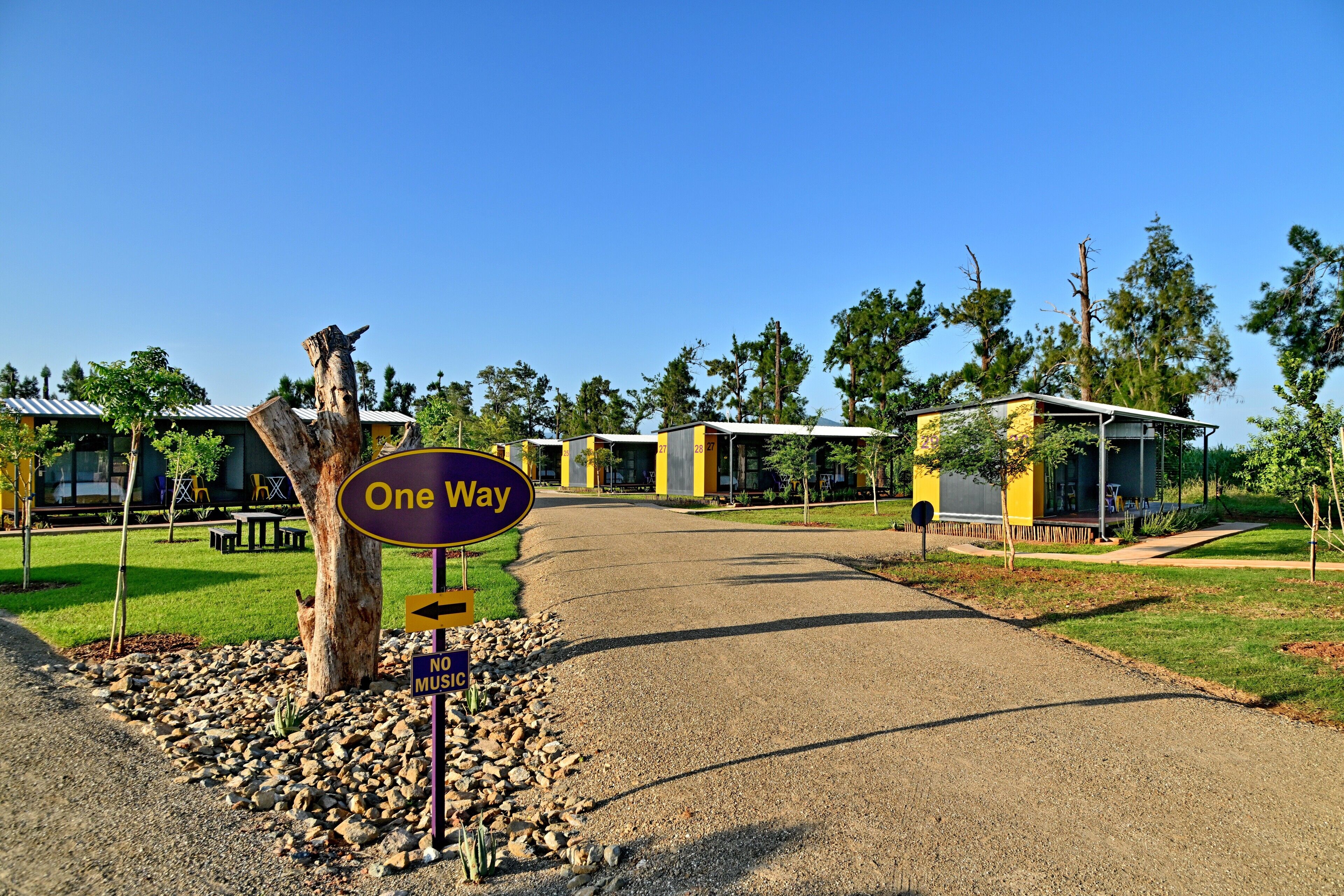 A one-way street leading to a building with a yellow and gray facade, surrounded by trees and a clear sky.