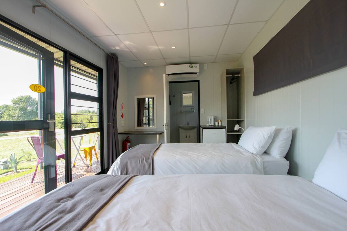 A hotel room with two beds, a bathroom, and a balcony with chairs.