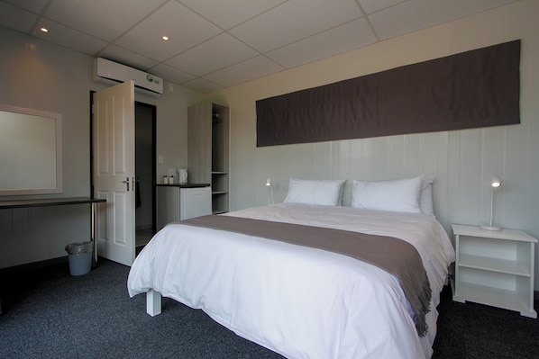 A hotel room with a large bed, a bedside table, a nightstand, a wardrobe, and a mirror.