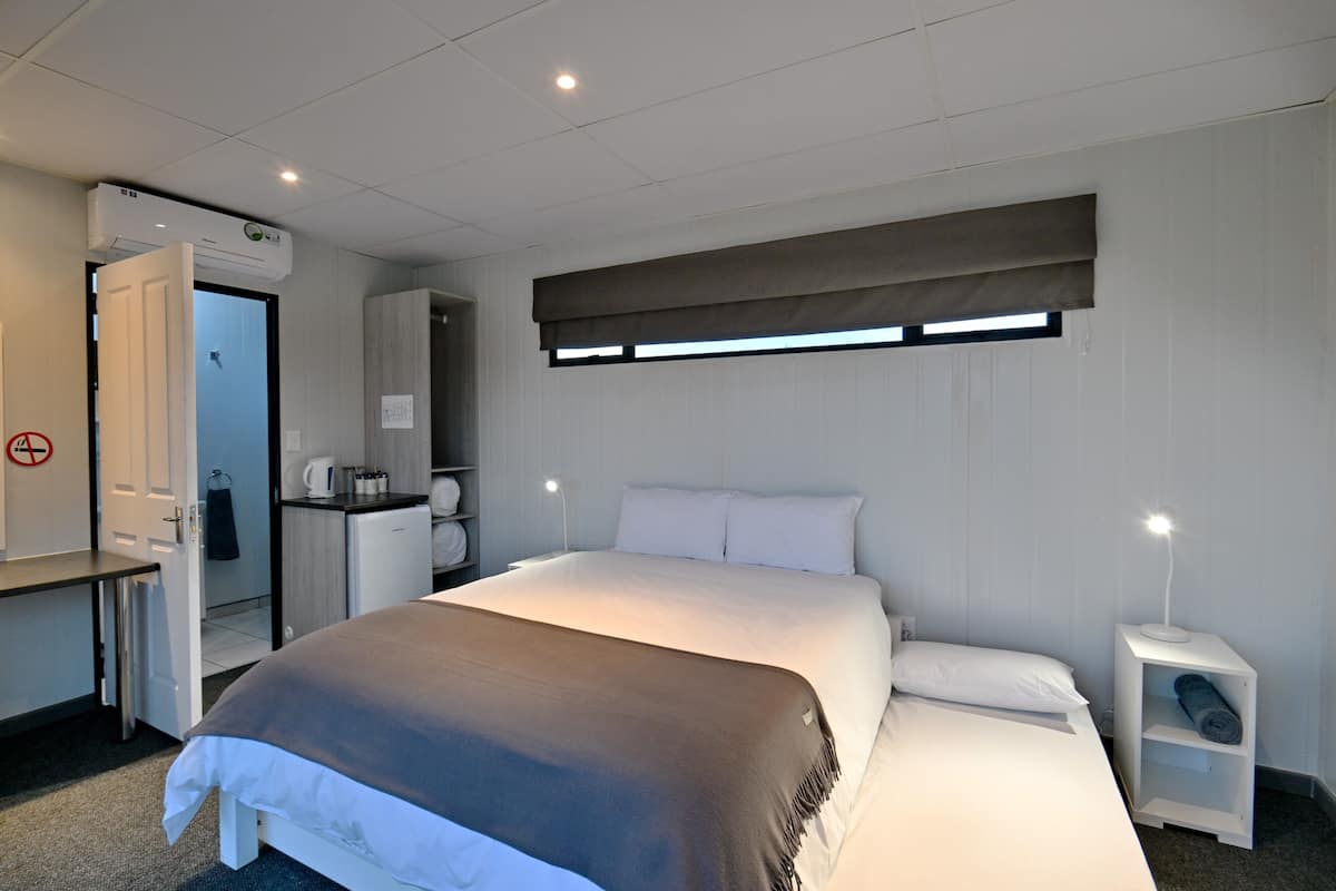A hotel room with a bed, bedside table, nightstand, and a window with blinds.