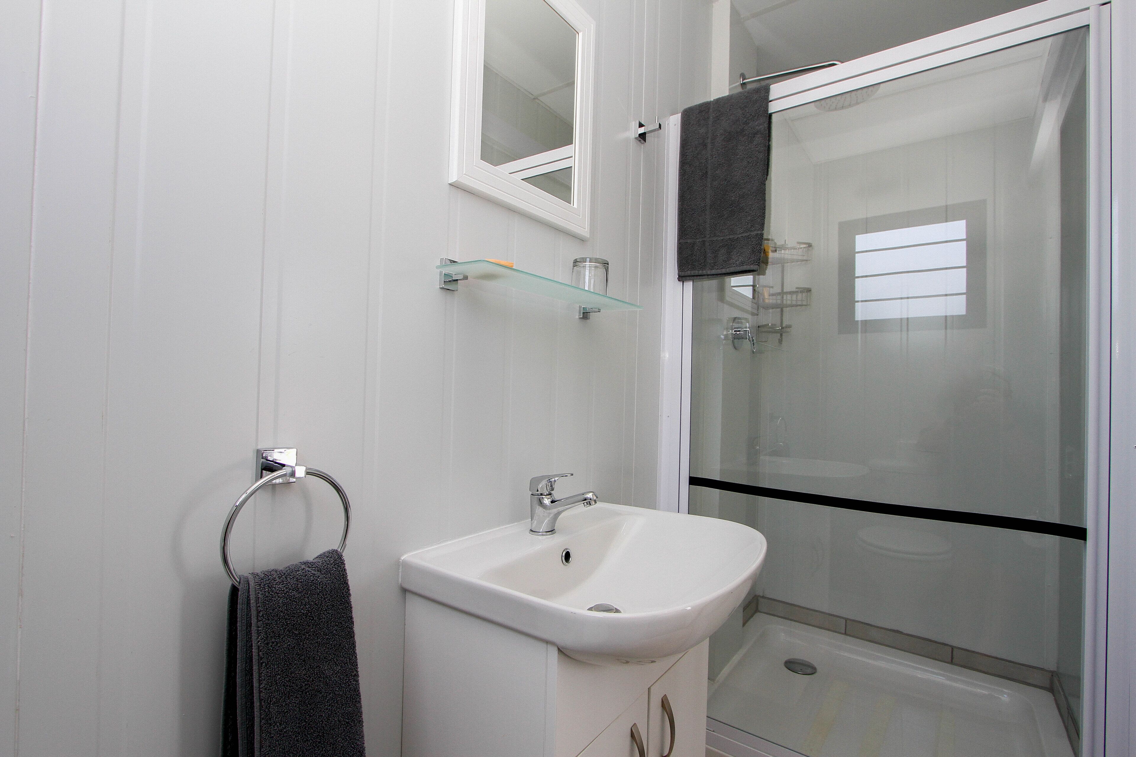 A bathroom with a white sink, a glass shelf, a towel ring, and a glass shower enclosure.
