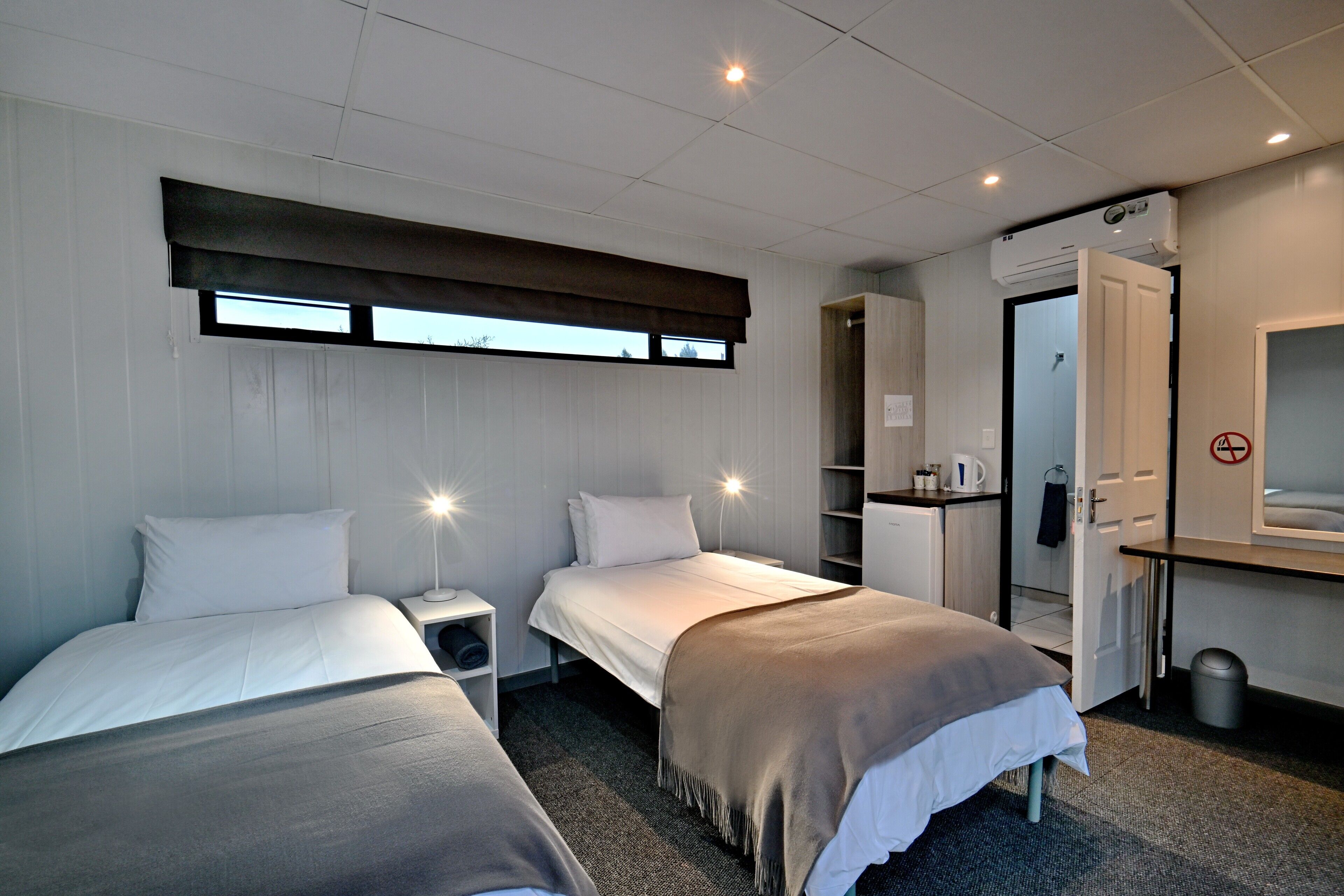 A hotel room with two beds, a desk, a wardrobe, and a window with a view.