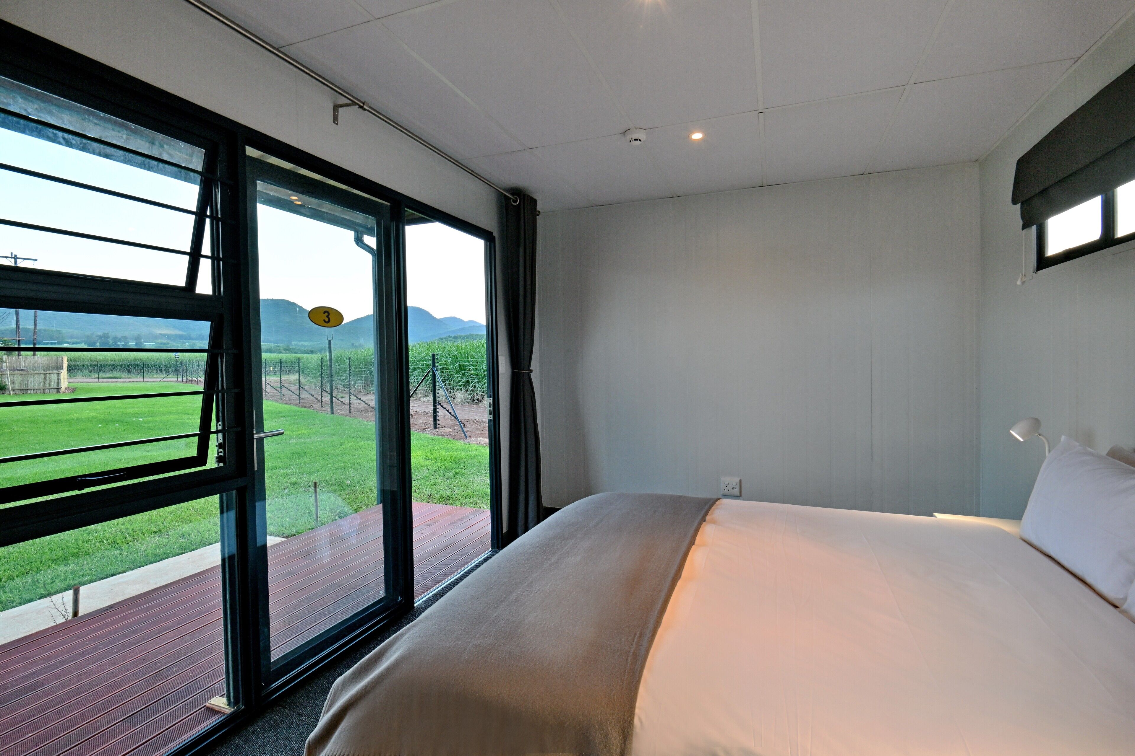 Ein Schlafzimmer mit einem großen Bett, Blick auf eine grüne Landschaft durch ein Fenster und eine Holzterrasse draußen.