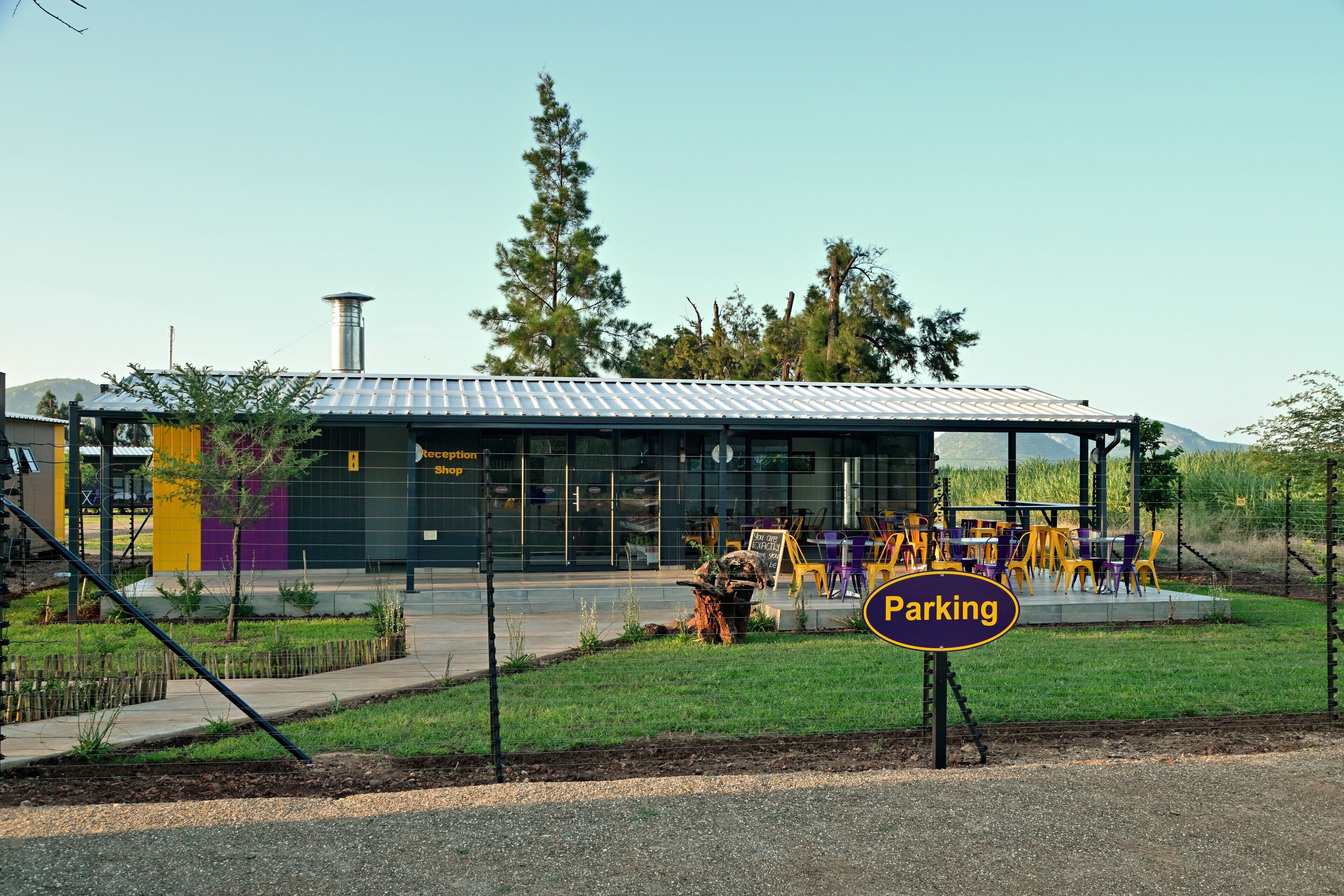 A building with a glass facade, a parking sign, and outdoor seating with yellow chairs.
