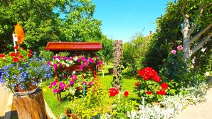 Een tuin met een houten pergola, verschillende bloeiende planten en een boomstam.