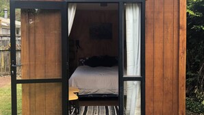 A wooden cabin with a "Welcome" sign, a bed, and a small table.