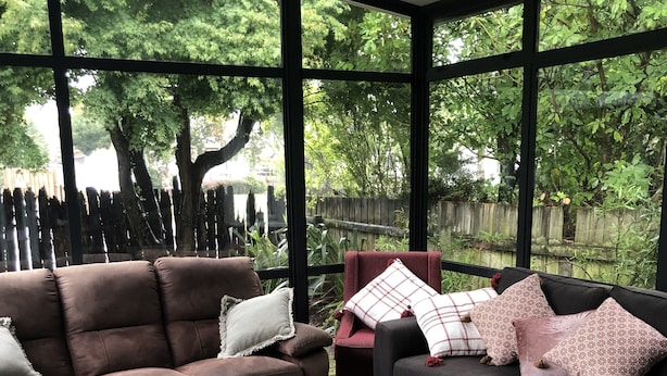 A conservatory with two sofas, a patterned rug, and a view of a wooded area through large windows.