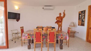 A dining area with a table set for six, surrounded by wooden chairs with red cushions. An air conditioning unit is mounted on the wall above the table. - Holiday apartment with sea views near the beach (Pješćana Uvala)