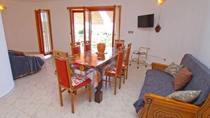 A living room with a dining table, chairs, a sofa, and a TV mounted on the wall. - Holiday apartment with sea views near the beach (Pješćana Uvala)