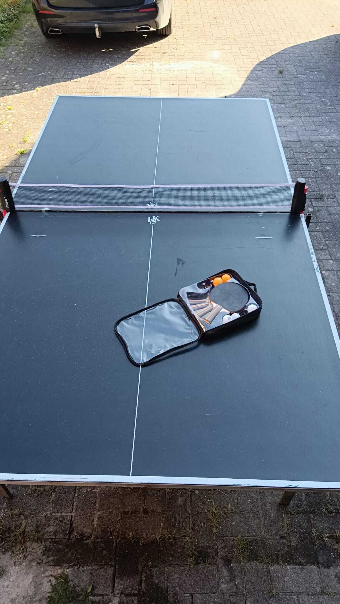 A ping pong table with a case containing balls and a paddle.