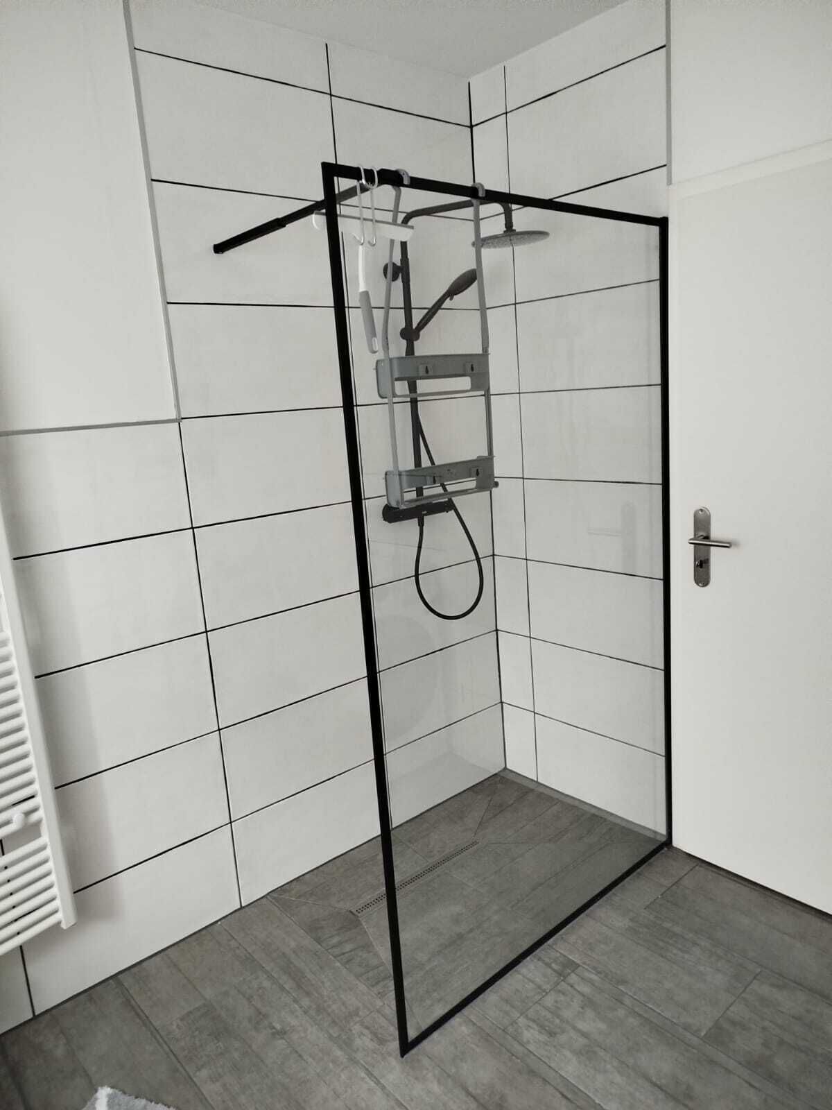 Un box de ducha moderno con puerta de vidrio, un perchero y un cabezal de ducha.