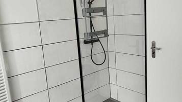 Un box de ducha moderno con puerta de vidrio, un perchero y un cabezal de ducha.