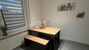 A small, modern room with a wooden table and bench, a radiator, and a window with blinds. - Modern and family-friendly: 3 bedrooms in Burhave (6 pers. plus baby crib) (Butjadingen)