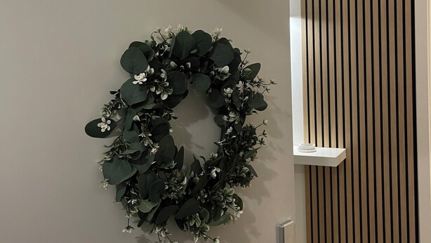 A door with a green wreath, a vertical wooden panel, and a white shelf. - Modern and family-friendly: 3 bedrooms in Burhave (6 pers. plus baby crib) (Butjadingen)