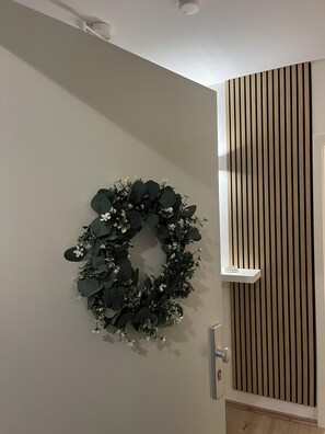 A door with a green wreath, a vertical wooden panel, and a white shelf.