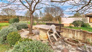 A patio area with a stone table and a white chair, surrounded by a stone wall and various plants.