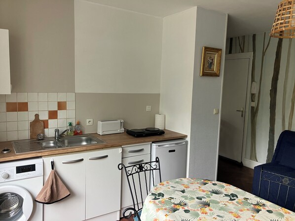Eine kleine Küche mit Spüle, Toaster und Geschirrspüler. Im Vordergrund stehen ein Stuhl und ein Tisch.