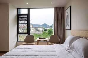 A hotel room with a large bed, two chairs, a small table, and a window offering a city view. - Wuyishan Yunzhong Jinshu Homestay (Wuyishan)