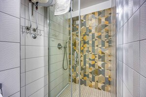 Eine Dusche mit geometrischem Fliesenspiegel, einer Glastür und einem Handtuch an einem Haken.