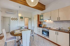 Une cuisine avec des meubles blancs, un four à micro-ondes, une cuisinière et un évier. On y trouve également une table à manger avec des chaises.