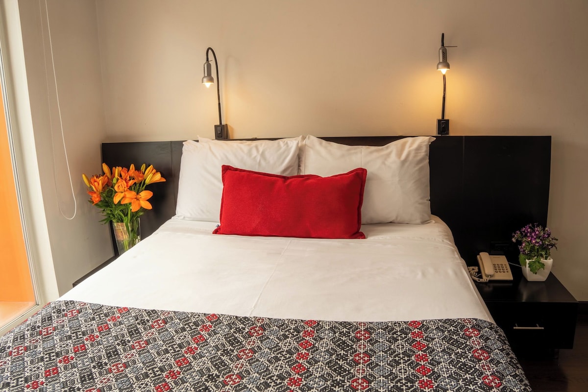 Une chambre d’hôtel avec un lit, deux lampes de chevet, une table de chevet avec un téléphone et un vase rempli de fleurs.