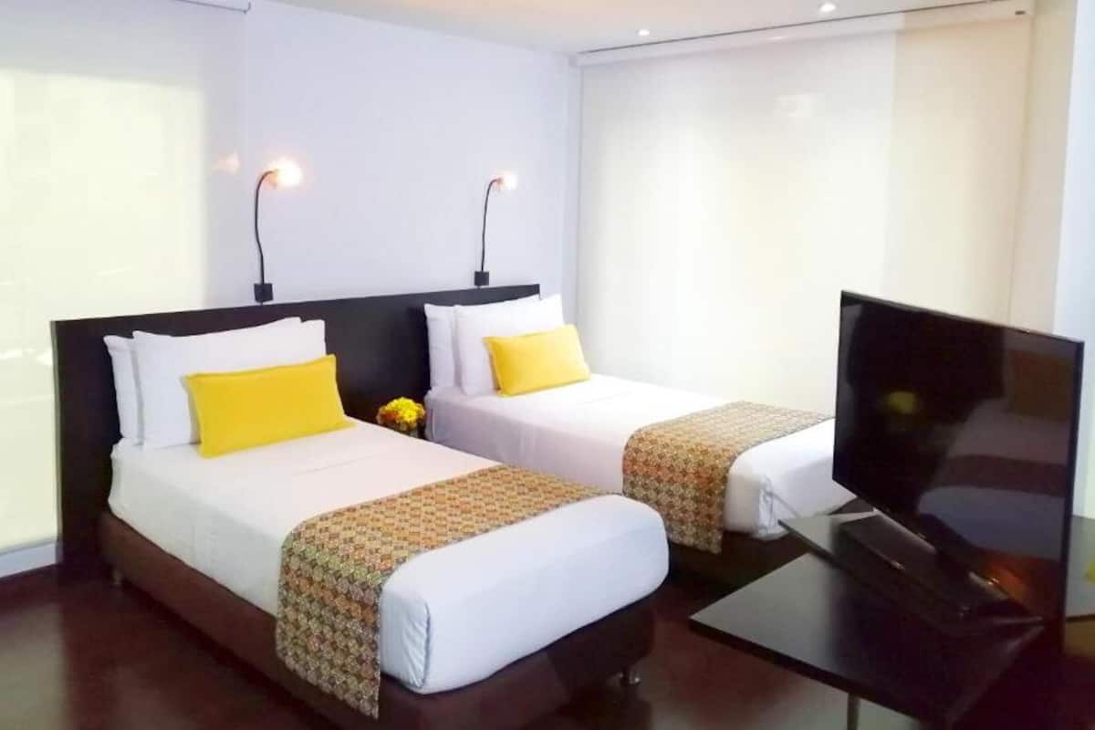 Quarto de hotel com duas camas, televisão e janela com cortinas.