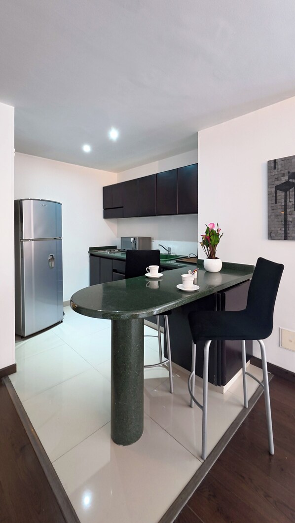 Cocina moderna con isla central, armarios negros y electrodomésticos de acero inoxidable.
