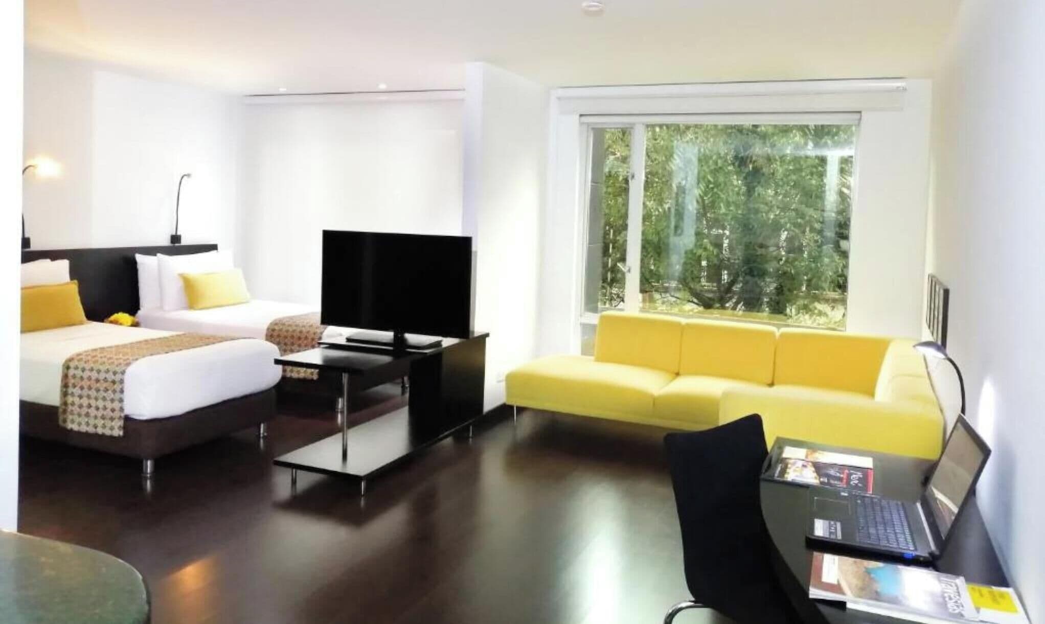 Een moderne hotelkamer met een bed, een televisie, een bank en een bureau met een laptop.