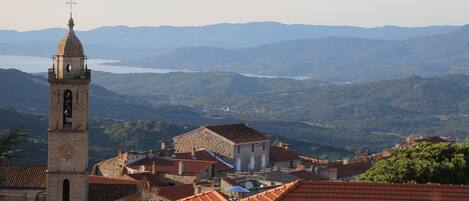 A historic town with a prominent clock tower, terraced roofs, and a mountainous backdrop.