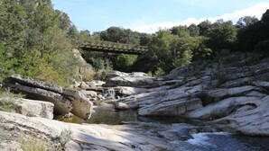 A rocky riverbed with a small waterfall and a bridge in the background.