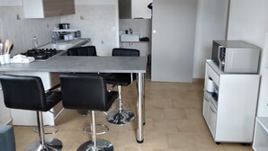 A compact kitchen with a central island, black bar stools, a microwave, and a stove.