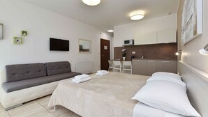 Une chambre d’hôtel moderne équipée d’un lit, d’un canapé, d’un petit coin cuisine et d’une télévision.