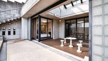 A modern building with a covered outdoor area, a staircase, and a seating area with tables and chairs.