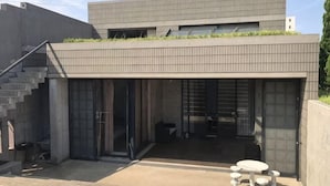 A modern building with a flat roof, a staircase on the left, and a covered outdoor seating area with tables and chairs. - BRUCE HOUSE (Izumisano)