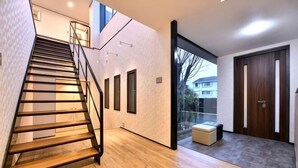 A modern interior with a wooden staircase, a glass door leading outside, and a small seating area. - BRUCE HOUSE (Izumisano)