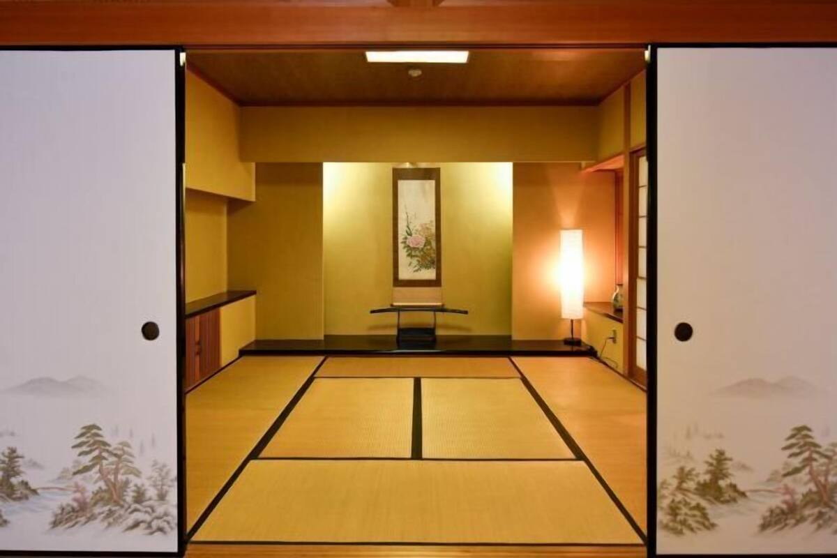 Una habitación japonesa tradicional con suelo de tatami, un biombio shoji, un pergamino colgado y una mesa baja.