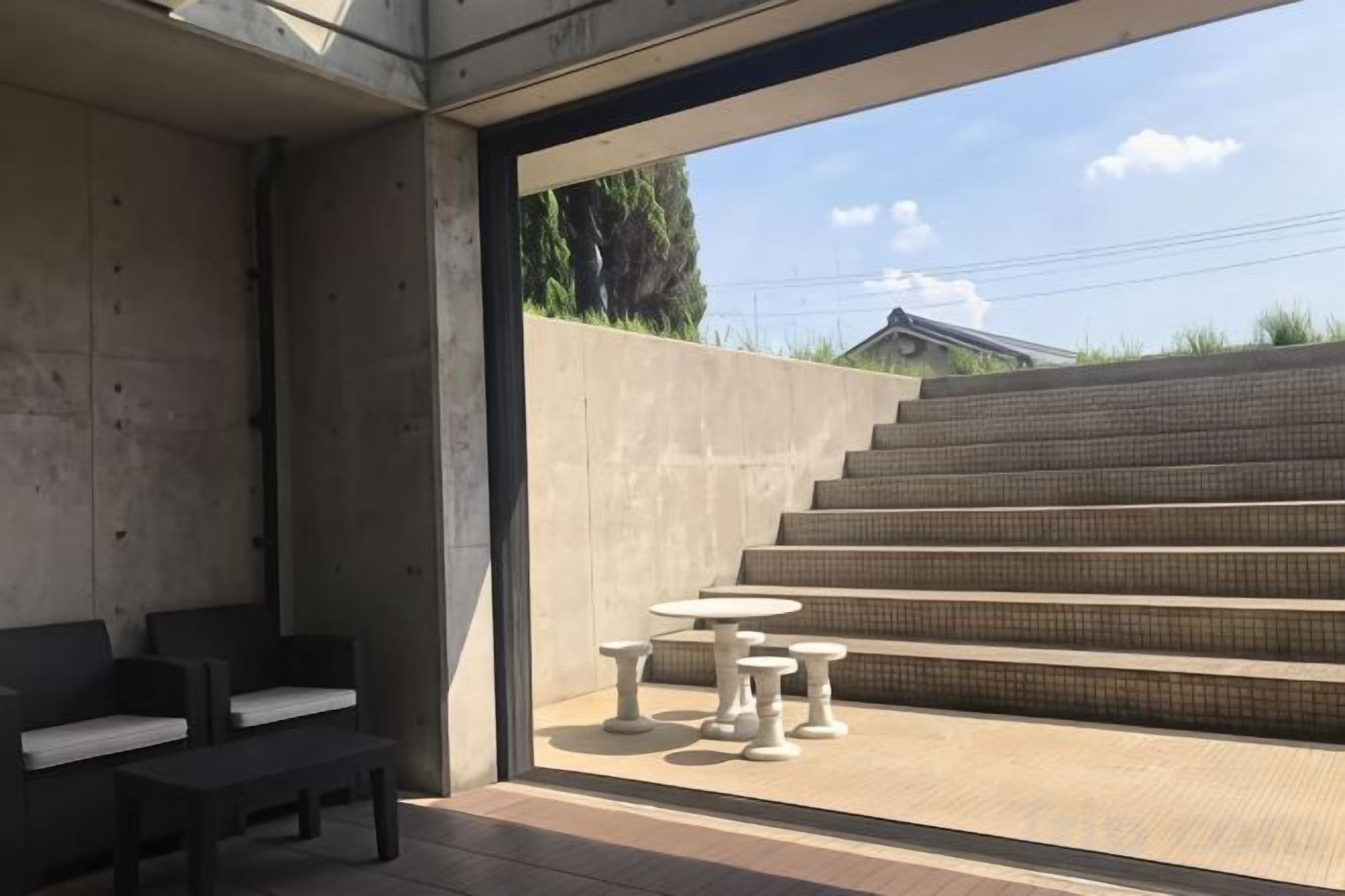 A modern outdoor seating area with concrete walls, a staircase, and a view of a residential building.
