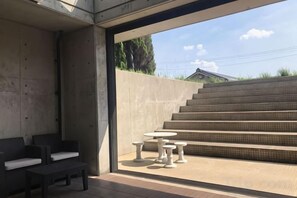 A modern outdoor seating area with concrete walls, a staircase, and a view of a residential building. - BRUCE HOUSE (Izumisano)