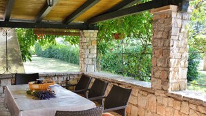 Une terrasse extérieure avec des murs en pierre, un espace salon abrité et une vue sur un jardin.