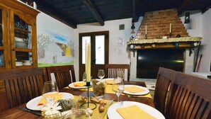 Un coin repas avec une table en bois dressée pour quatre personnes, entourée de chaises en bois. On aperçoit une cheminée en briques au fond.
