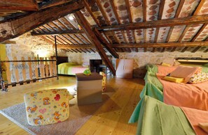 A rustic attic bedroom with exposed wooden beams, a stone wall, a bed with green and pink bedding, a small table, and a wooden bench with a cartoon pattern. - Holiday home with pool for 8 people (Vodnjan)
