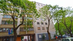A multi-story building with a flat facade, several windows, and a parking area with cars and trees.