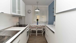 A compact kitchen with white cabinetry, a stainless steel sink, a hanging pendant light, and a clock on the wall.