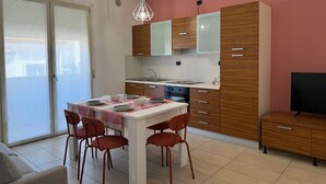 A modern kitchen with wooden cabinets, a white countertop, and a dining area with a table and chairs. - Bavierino in Cattolica (Cattolica)