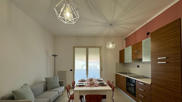 A modern kitchen with wooden cabinets, a dining table with chairs, and pendant lighting. - Bavierino in Cattolica (Cattolica)