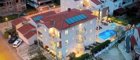 A multi-story hotel with a swimming pool, balconies, and a well-lit entrance.