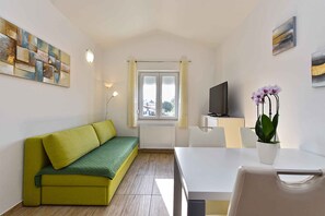 Een moderne woonkamer met een groene bank, een witte tafel, een televisie en een kamerplant.