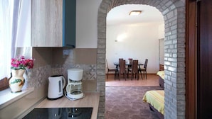A kitchen with a coffee maker, a kettle, and a vase with flowers on the counter. There is a dining area with a table and chairs visible through an archway. - Holiday apartment near the beach (Pješćana Uvala)